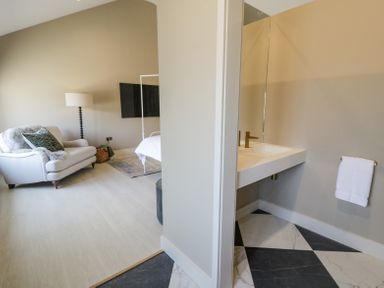 A bedroom with a chair and a bed next to a bathroom sink with a mirror and towel at The Barn in Llanfechell