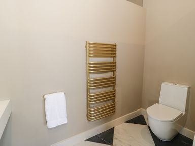 A bathroom with a white toilet a gold towel heater and a white towel on a rack at The Barn in Llanfechell