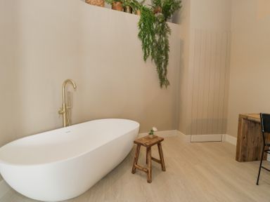 A bathroom with a white freestanding bathtub wooden stool and hanging plants at The Barn in Llanfechell