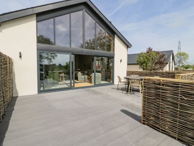 An outdoor patio area with a table and chairs outside a building with large glass windows at The Barn in Llanfechell