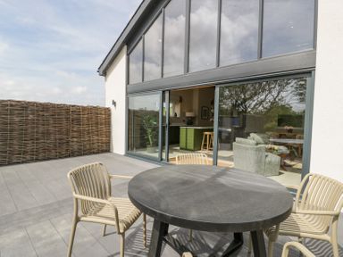 An outdoor patio with a round table and four chairs next to large sliding glass doors at The Barn in Llanfechell