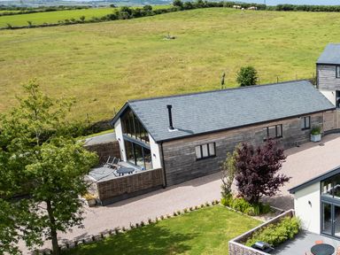 A long single-story building with large windows and a patio area in a rural setting at The Barn in Llanfechell
