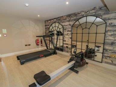 A gym room with a treadmill and rowing machine and large mirrors on the wall at Farmyard House Llanfechell