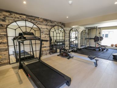 A home gym with a treadmill rowing machine weight bench and mirrors at Farmyard House in Llanfechell