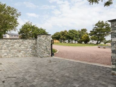 An outdoor area with stone wall pillars paving and a gravel driveway with trees in the background at Farmyard House in Llanfechell