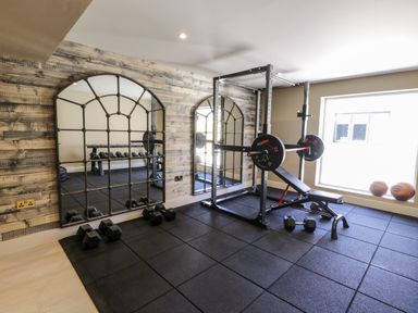 A home gym with weightlifting equipment dumbbells and a bench near a window at Farmyard House in Llanfechell