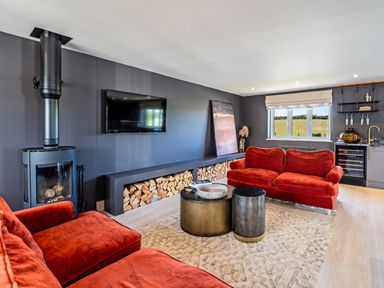 A living room with red sofas a wood burning stove and a television at Farmyard House in Llanfechell
