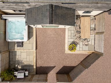An outdoor patio area with a hot tub wooden dining table with chairs and a barbecue grill at Farmyard House Llanfechell