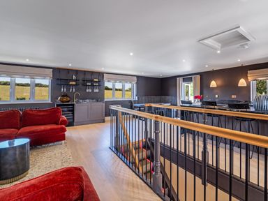 An upper floor lounge area with red sofas a bar counter stools and windows showing a field at Farmyard House in Llanfechell