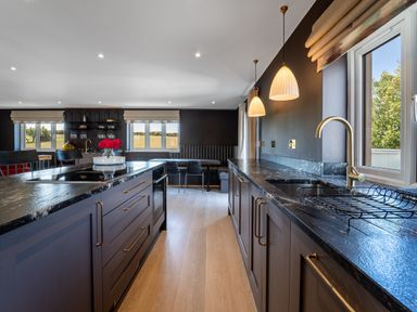 A kitchen with dark cabinets and countertops with pendant lights above at Farmyard House in Llanfechell