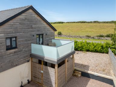 A wooden house with a balcony with frosted glass panels and a gravel yard at Farmyard House in Llanfechell