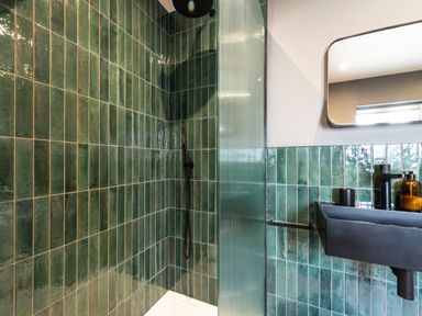 A bathroom with green tiled walls a black sink and shower area at Farmyard House in Llanfechell