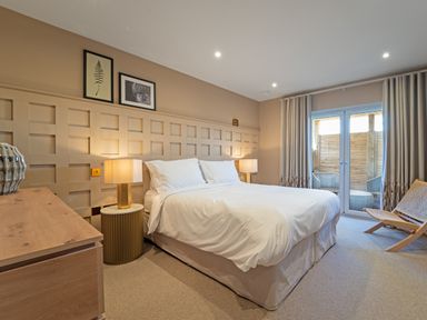 A bedroom with a bed between two lamps and a door leading to an outdoor seating area at Farmyard House in Llanfechell