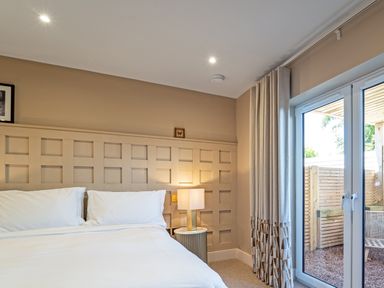 A bedroom with a bed side table lamp and curtains beside glass doors at Farmyard House in Llanfechell