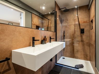 A bathroom with a double sink and black fixtures next to a walk-in shower with brown tiled walls at Farmyard House in Llanfechell