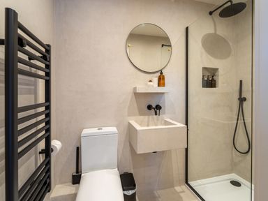A bathroom with a toilet sink round mirror shower enclosure and towel rack at Farmyard House in Llanfechell
