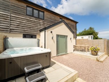An outdoor patio area with a hot tub and a dining table with chairs at Farmyard House in Llanfechell