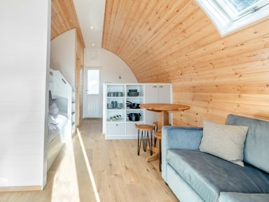 A living space with a sofa a round wooden table stools built in shelves and a wooden curved ceiling at Carlton Manor Pod 1 in Aldbrough