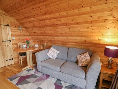 A living room with a gray sofa wooden dining table with chairs and a lamp on a side table at Pine Lodge in Llanddeusant near Llandovery