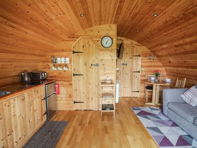 A wooden cabin interior with kitchenette, dining table, sofa, and two wooden doors at Pine Lodge in Llanddeusant near Llandovery