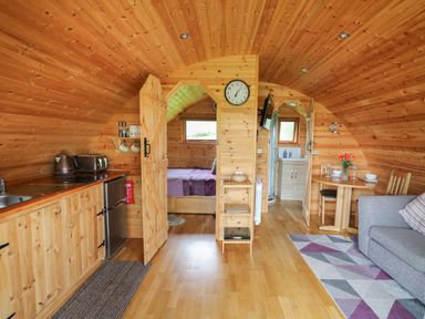 An interior view of a wooden cabin with a kitchenette on the left a bedroom in the middle and a bathroom on the right with a dining table and sofa at Pine Lodge in Llanddeusant near Llandovery