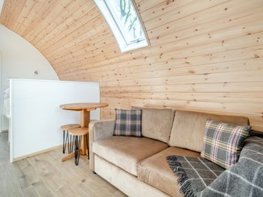 A curved wood-paneled room with a beige sofa and a small round wooden table with two stools at Carlton Manor Pod 2 in Aldbrough
