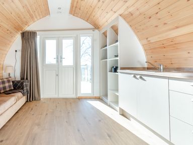 A small living area with a sofa a floor lamp kitchen cabinets and shelves near double doors at Carlton Manor Pod 2 in Aldbrough