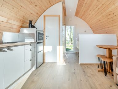 A kitchen area with cabinets microwave and fridge next to a wooden dining table with stools in a pod accommodation at Carlton Manor Pod 2 Aldbrough