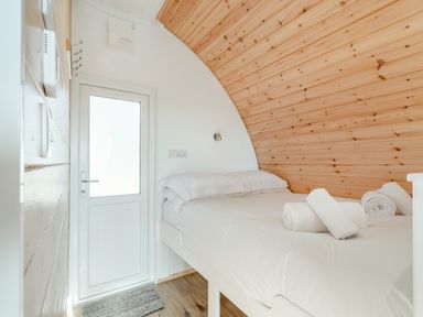 A bedroom with a double bed white linens rolled towels wooden curved ceiling and a white door at Carlton Manor Pod 2 Aldbrough
