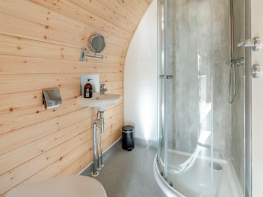 A bathroom with a wooden wall panel a small sink a round shower enclosure and a trash bin at Carlton Manor Pod 2 in Aldbrough