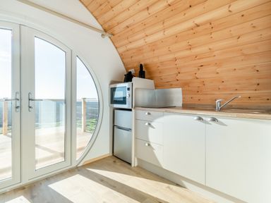 A small kitchen area with a microwave refrigerator and sink next to large circular glass doors at Carlton Manor Pod 8 in Aldbrough