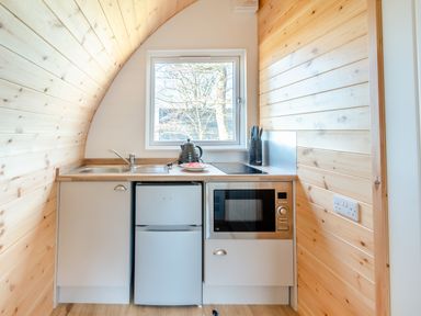 A compact kitchen with a sink, kettle, knives, refrigerator, and microwave beneath a window at Carlton Manor Pod 10 in Aldbrough
