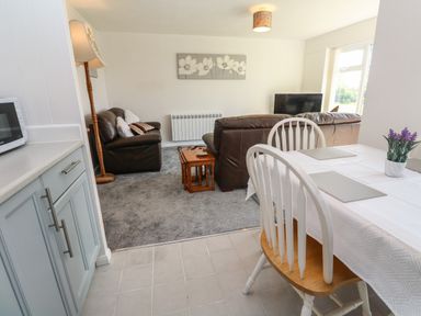 A dining table with chairs and a living room with sofas and a TV at 39 Manorcombe Bungalows in Honicombe Holiday Village near Drakewalls