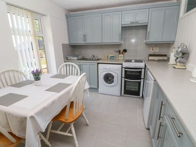 A kitchen with blue cabinets a dining table with chairs and appliances at 39 Manorcombe Bungalows in Honicombe Holiday Village near Drakewalls