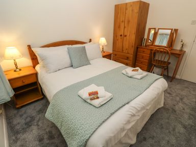 A bedroom with a bed a wooden wardrobe a dressing table with mirror and chair at 39 Manorcombe Bungalows Honicombe Holiday Village near Drakewalls