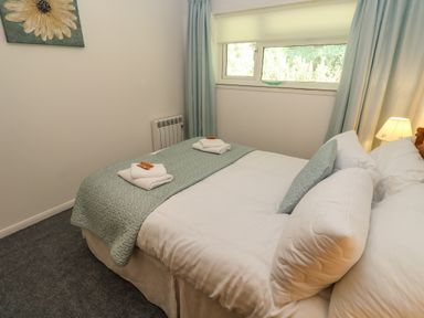 A bedroom with a double bed two folded towels and a window at 39 Manorcombe Bungalows in Honicombe Holiday Village near Drakewalls