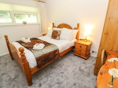 A bedroom with a wooden bed side tables a desk chair and a window at 39 Manorcombe Bungalows in Honicombe Holiday Village near Drakewalls