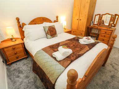 A bedroom with a wooden bed two bedside tables a wardrobe and a dressing table with a chair at 39 Manorcombe Bungalows Honicombe Holiday Village near Drakewalls