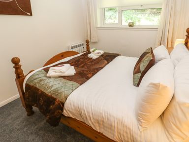 A bedroom with a wooden bed with white bedding and brown decorative pillows at 39 Manorcombe Bungalows in Honicombe Holiday Village near Drakewalls