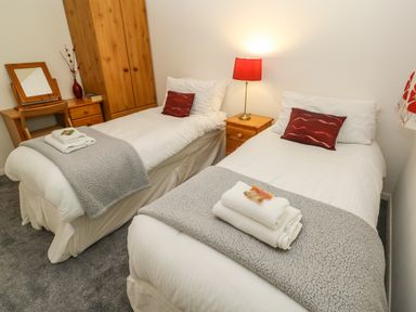 A bedroom with two single beds with white bedding and grey throws at 39 Manorcombe Bungalows in Honicombe Holiday Village near Drakewalls