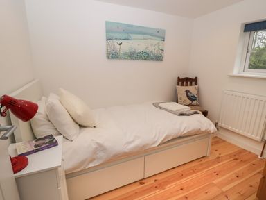 A small bedroom with a single bed a red desk lamp on a bedside table and a chair with a bird cushion at Brimley Barn in Kittisford near Milverton
