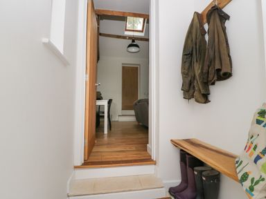 A hallway with coats hanging on hooks boots under a wooden bench and a view into a room with wooden flooring at Brimley Barn in Kittisford near Milverton