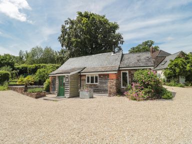 A small cottage with a green door gravel driveway and bushes at Brimley Barn in Kittisford near Milverton
