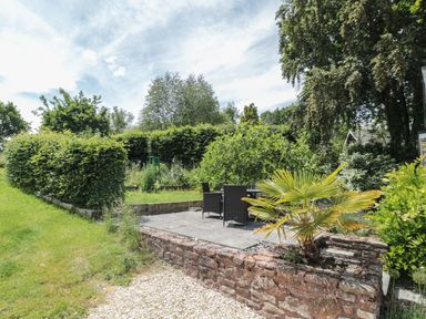 An outdoor patio with black chairs and table surrounded by green shrubs and trees at Brimley Barn Kittisford near Milverton