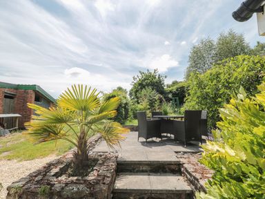 An outdoor patio with a table and four chairs surrounded by plants and trees at Brimley Barn Kittisford near Milverton