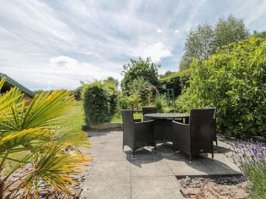 An outdoor patio area with a round table and four wicker chairs surrounded by plants and greenery at Brimley Barn in Kittisford near Milverton