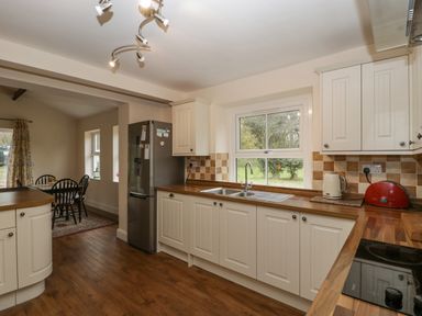 A kitchen with white cabinets wooden countertops a stainless steel refrigerator a sink under a window and a dining table with chairs at Heathfield in Milverton