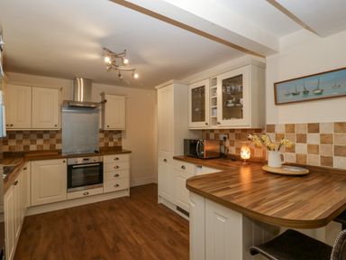 A kitchen with wooden countertops white cabinets a built in oven microwave flowers in a jug and a painting of boats at Heathfield in Milverton