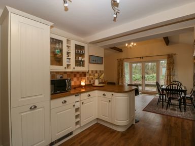 A kitchen with white cabinets and a wooden countertop next to a dining area with black chairs and glass doors at Heathfield Milverton