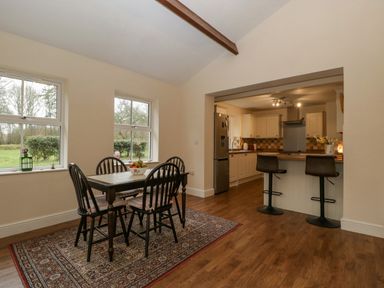 A dining area with a table and chairs on a rug next to windows connected to a kitchen with bar stools at Heathfield in Milverton
